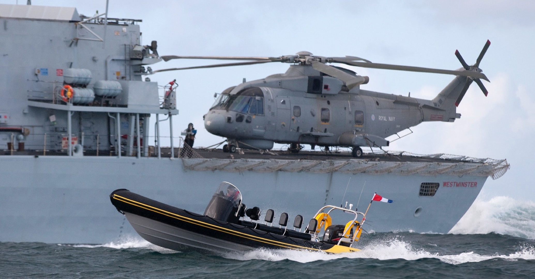 “Solent Rib Charter high-performance RIB operating alongside Royal Navy warship HMS Westminster with Merlin helicopter on deck during offshore operations.