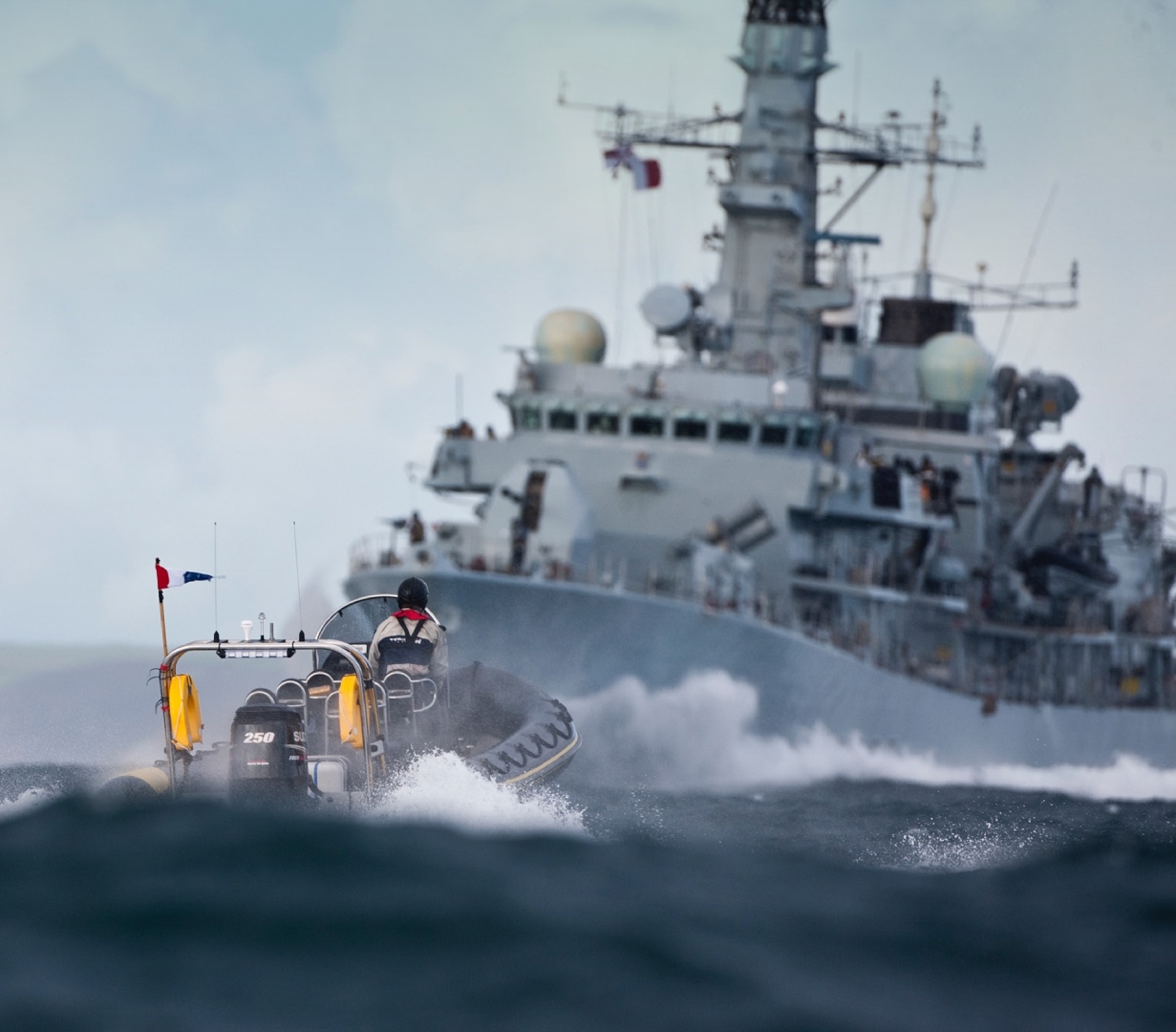 Solent Rib Charter high-speed RIB navigating rough seas in front of a Royal Navy warship during maritime operations