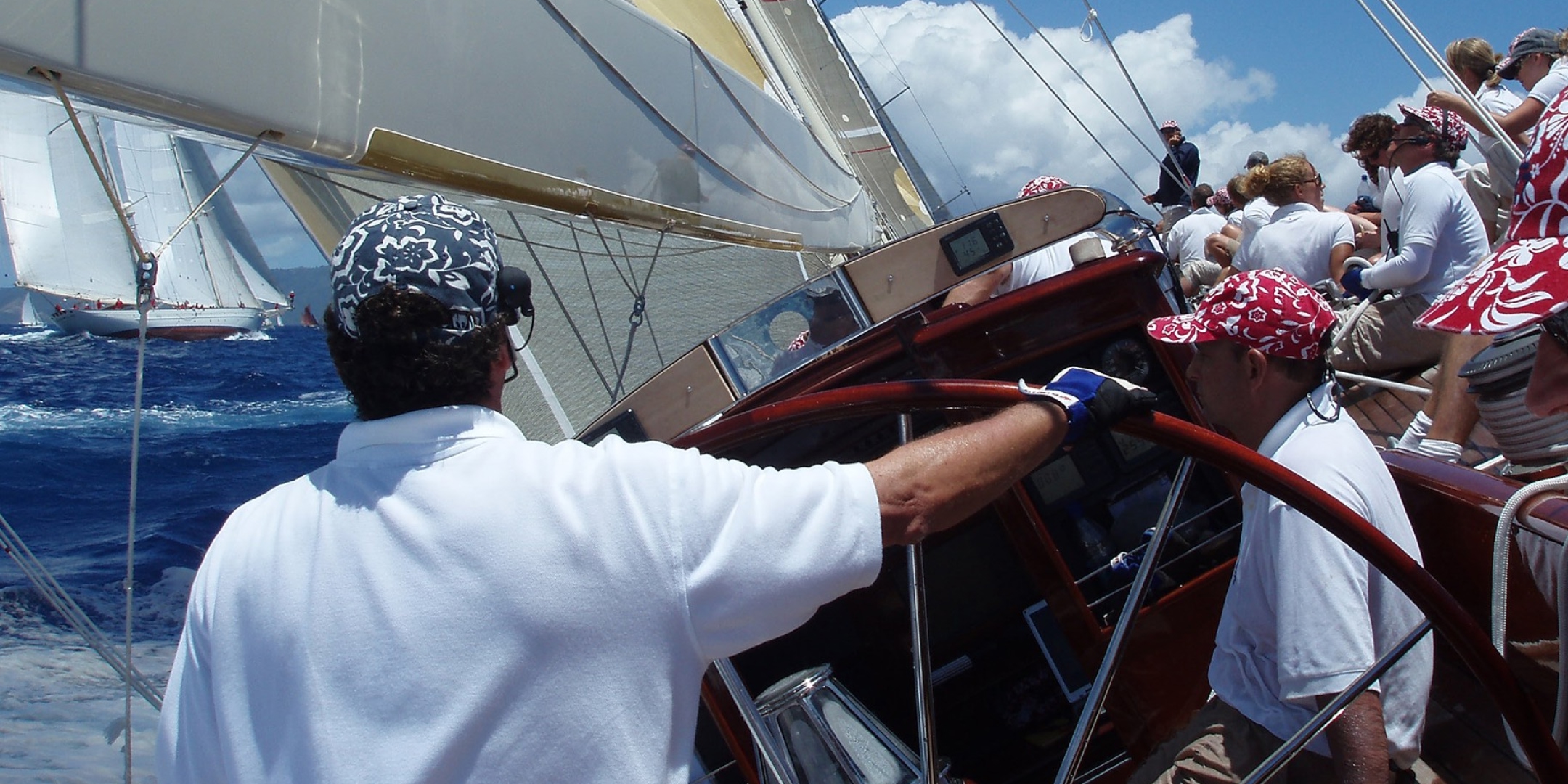 Crew members steering a classic racing yacht during an offshore sailing event, with sailors on deck and another yacht visible in the background – Solent Rib Charter marine experiences.