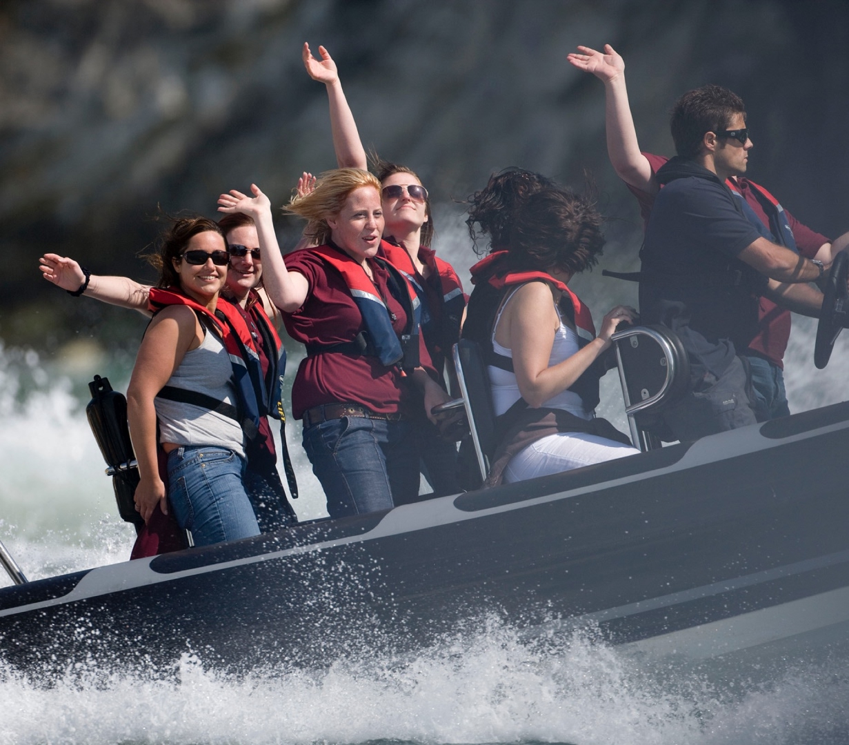 Group of people enjoying a high-speed RIB boat ride on the ocean, wearing life jackets and smiling as sea spray splashes around them