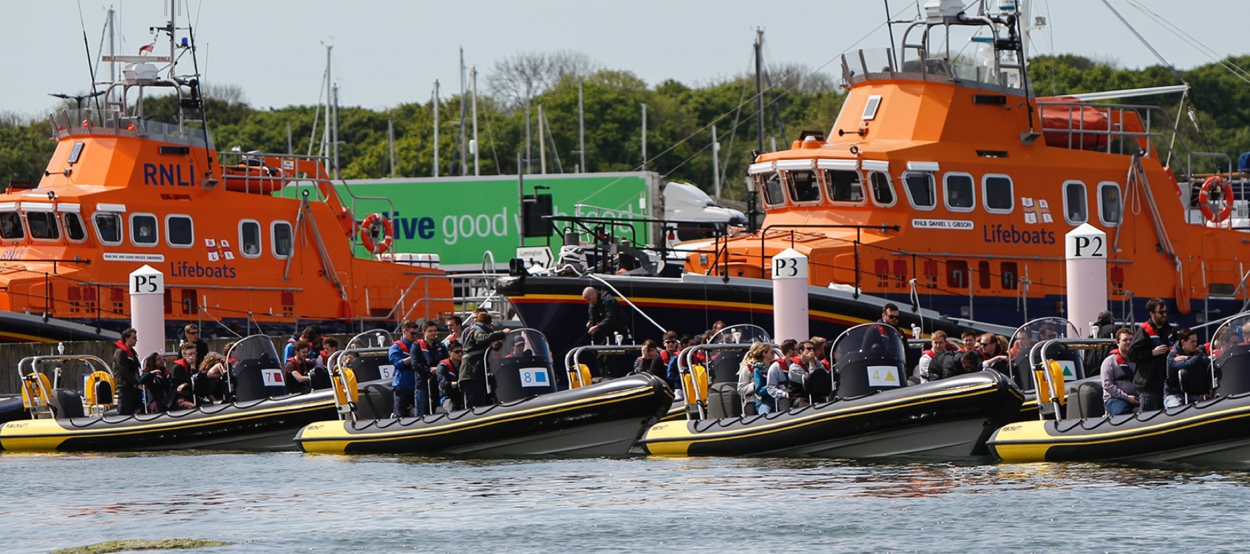Multiple Solent Rib Charter boats filled with passengers preparing to depart from the marina beside two RNLI lifeboats during a busy waterside event.