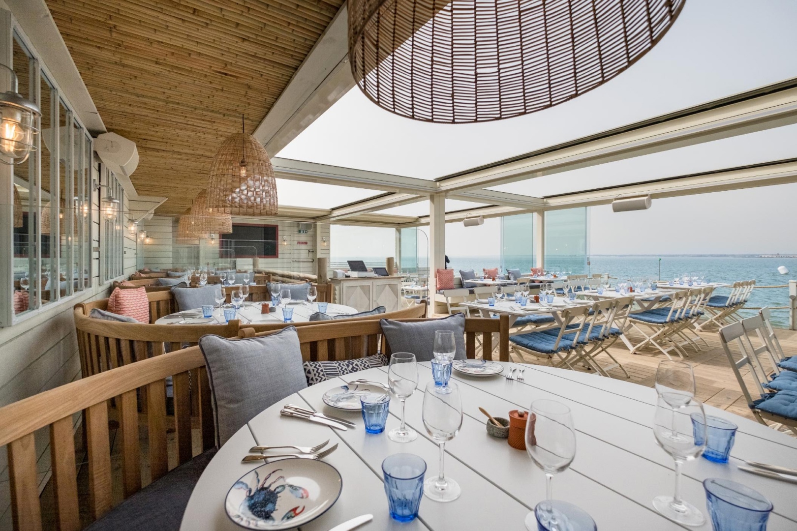 Bright coastal restaurant interior at The Hut in Colwell Bay with sea views, relaxed beach-house décor, and elegantly set dining tables.