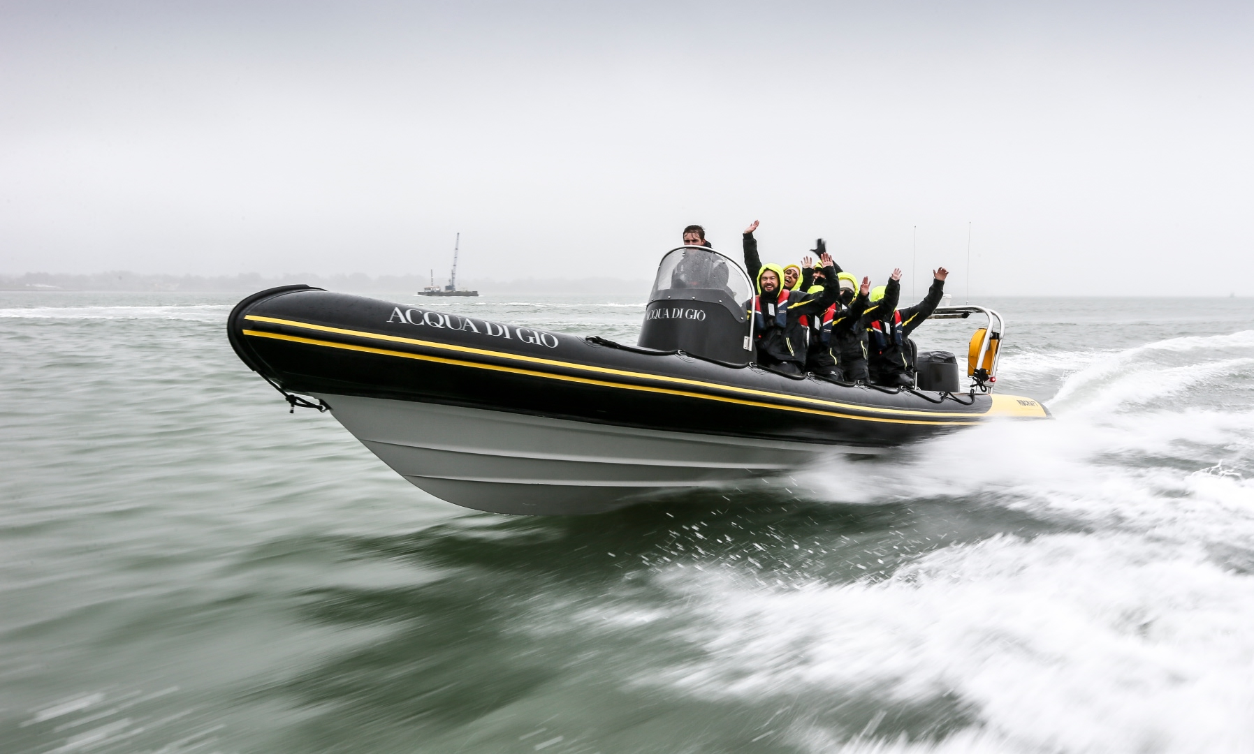 A fast-moving RIB with cheering passengers wearing bright hooded jackets on open water.