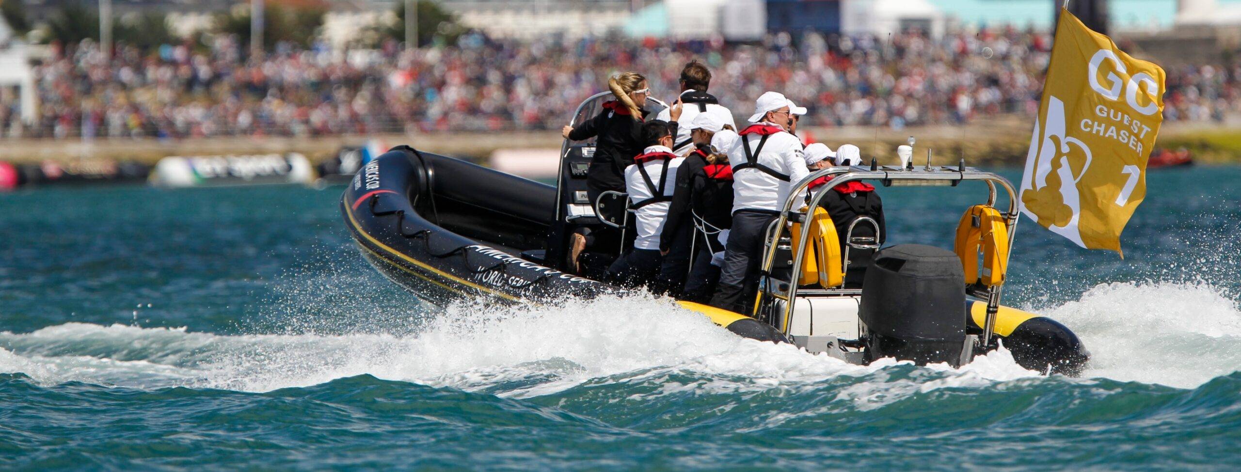 Solent Rib Charter Guest Chaser boat carrying spectators close to the America’s Cup racing action, speeding across the water with event crowds visible along the shore.