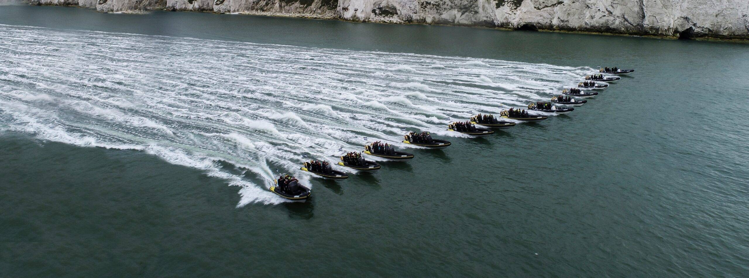 A formation of RIBs travelling together along the coastline, creating parallel wakes during a coordinated group experience.