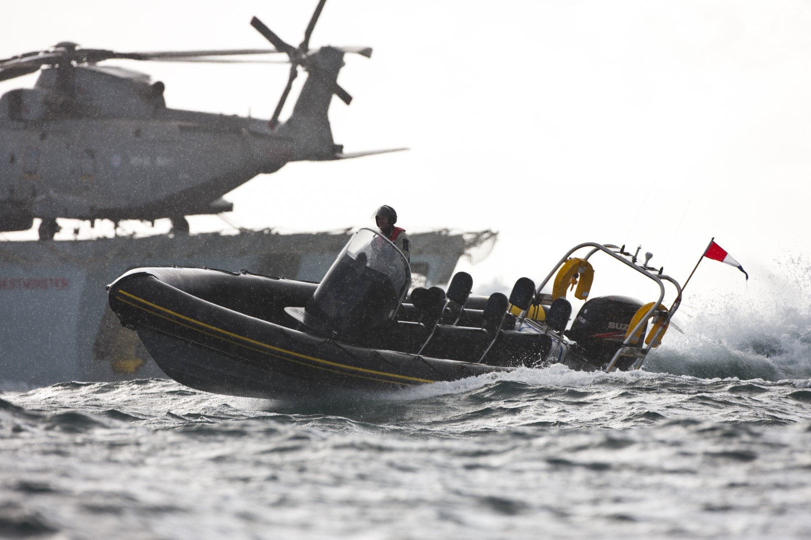 Rigid inflatable boat operating in rough seas with a helicopter on a ship in the background