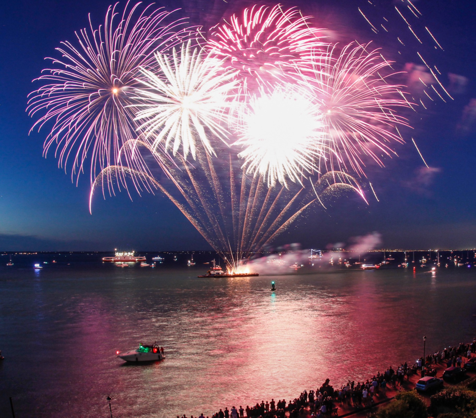 Fireworks display over water at night with boats and spectators watching